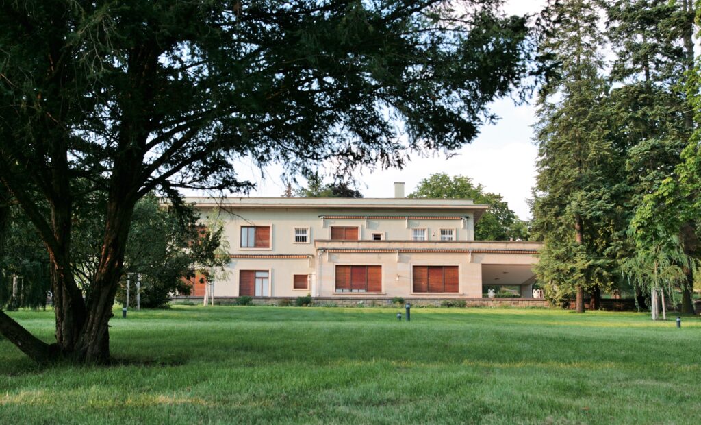 A modernist house can be seen through some trees and green grass. It's two stories and very clean. Wheely Tyred Brno hidden gems