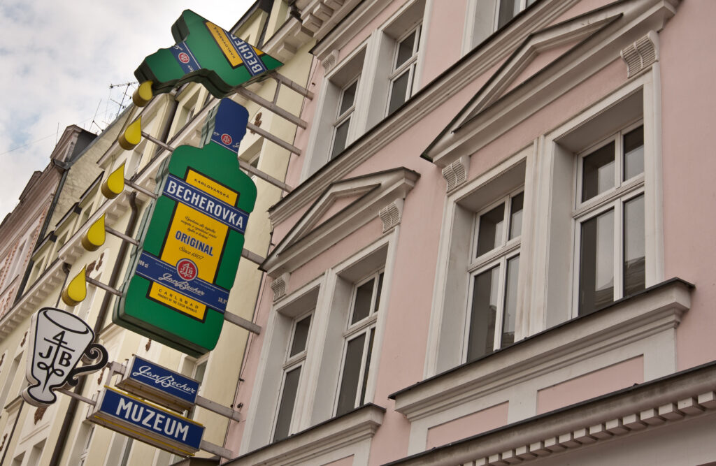 A sign hangs outside the Jan Becher Museum in Karlovy Vary. It looks like two bootles pouring a drink of Becherovka. Wheely Tyred top attractions in Karlovy Vary