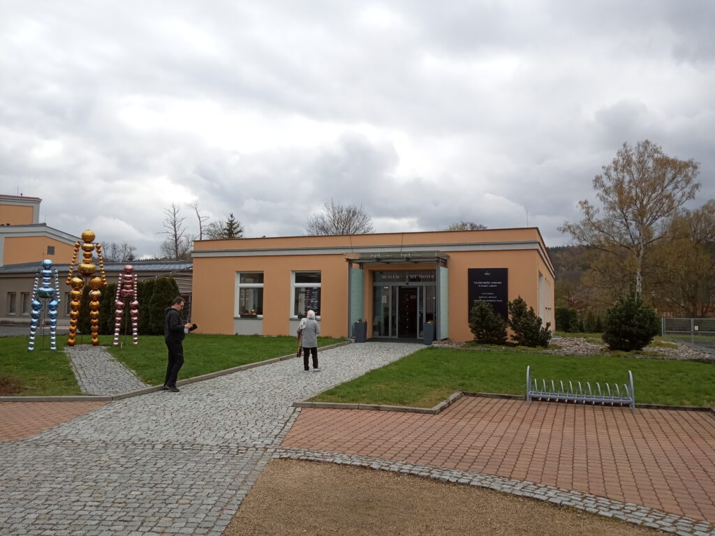 A small building on a grey day with the words: Moser Glassworks Museum, in Karlovy Vary. Wheely Tyred top attractions in Karlovy Vary