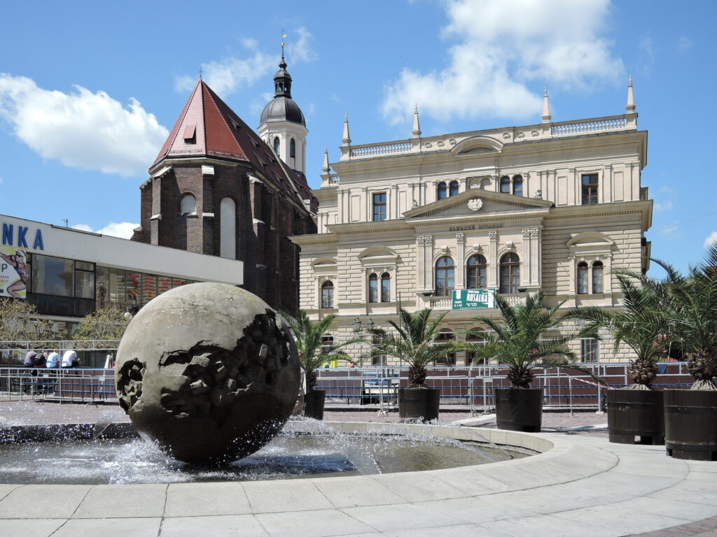 A sculpture sits in a square with a fountain, large ornate building and church in Horní náměstí, Opava. Wheely Tyred Czech Silesia attractions