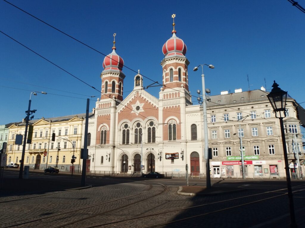 A large synagigue under a blue sky in font of tram lines in Plzen.