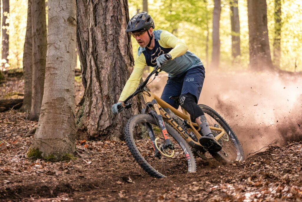 A man rides a mountain bike downhill through the woods, kicking up dust behind him. Wheely Tyred Czechia Cycling History