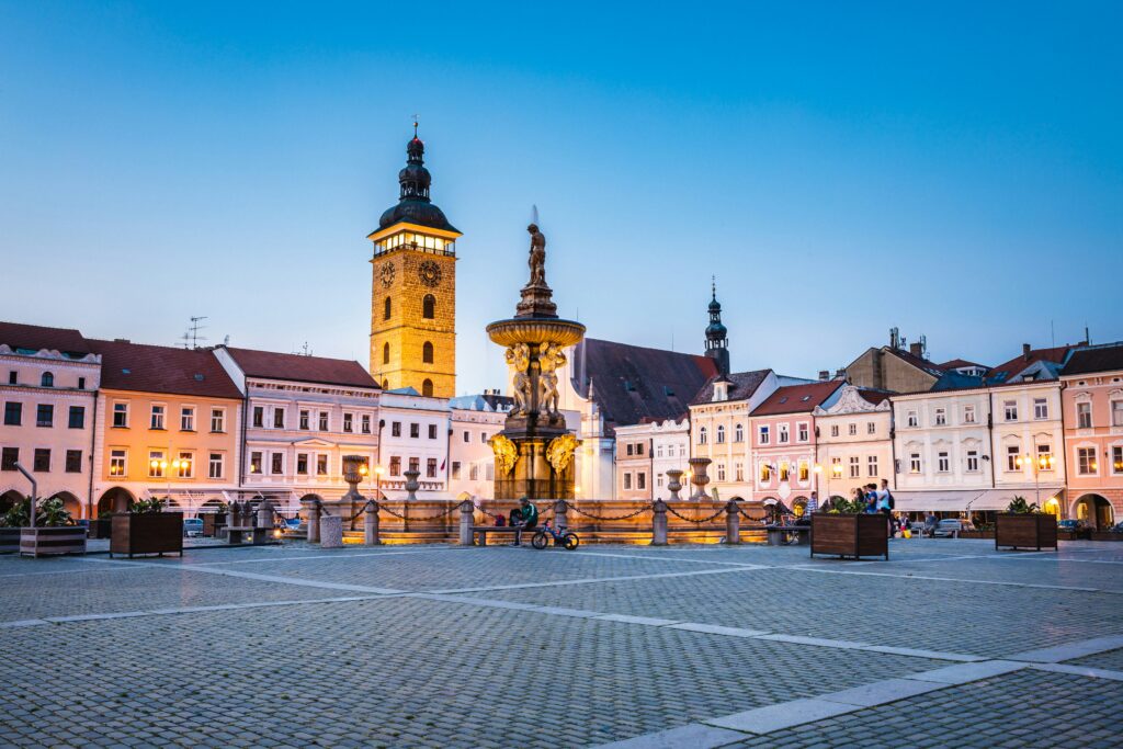 The huge Náměstí Přemysla Otakara II, or Přemysl Otakar II Square, in České Budějovice at dusk. Its churches, fountains and buildings are lit up.