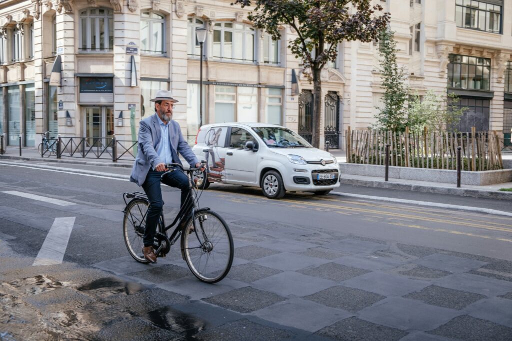 A man dressed stylish in a relaxed suit and hat rides a bike through Paris.