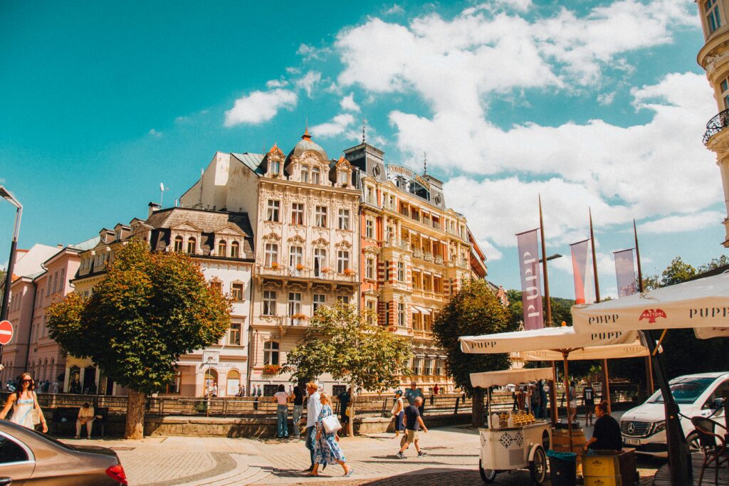 People walk past beautiful pastel-coloured Baroque buildings in a Czech city