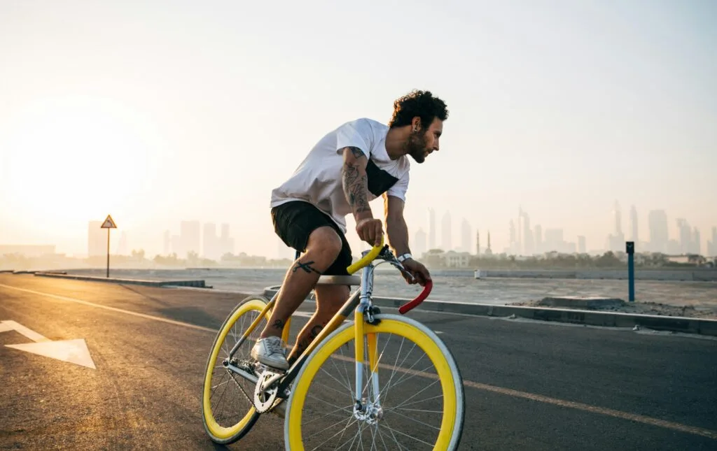 A man rides a yellow fixie bike along a coatal road with a city in the distance. Wheely Tyred cycling laws Czechia