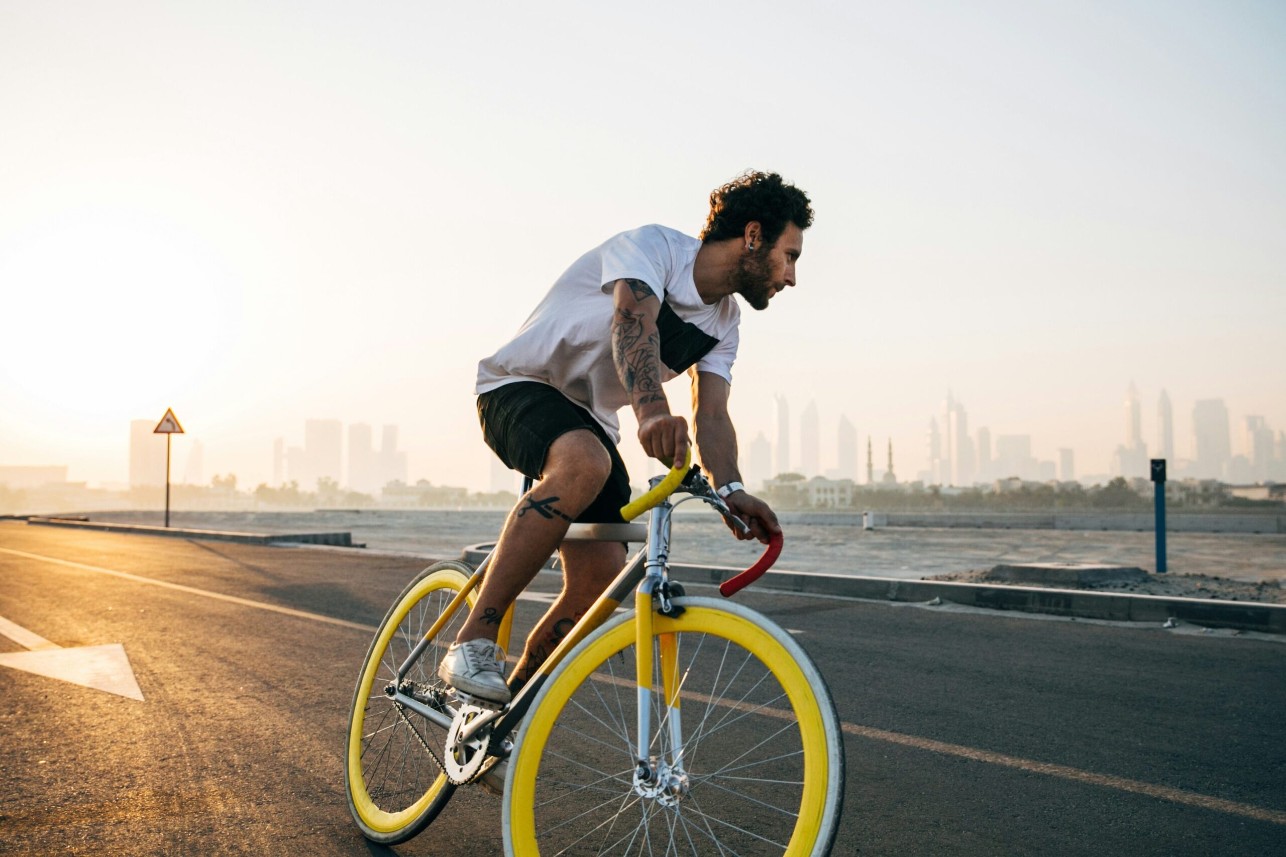 A man rides a yellow fixie bike along a coatal road with a city in the distance.