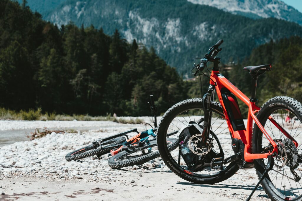 Two ebikes sit on a rocky plain near some pine covered mountains.