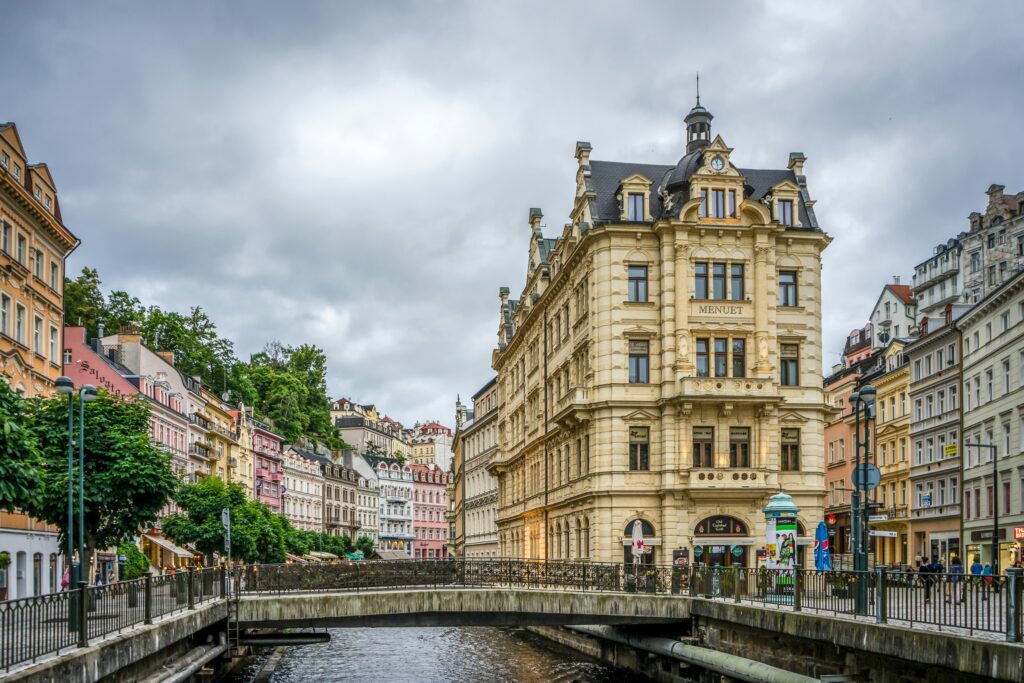 A bridge crosses a river in between the large, pastel-coloured buildings of Karlovy Vary. Wheely Tyred top attractions in Karlovy Vary