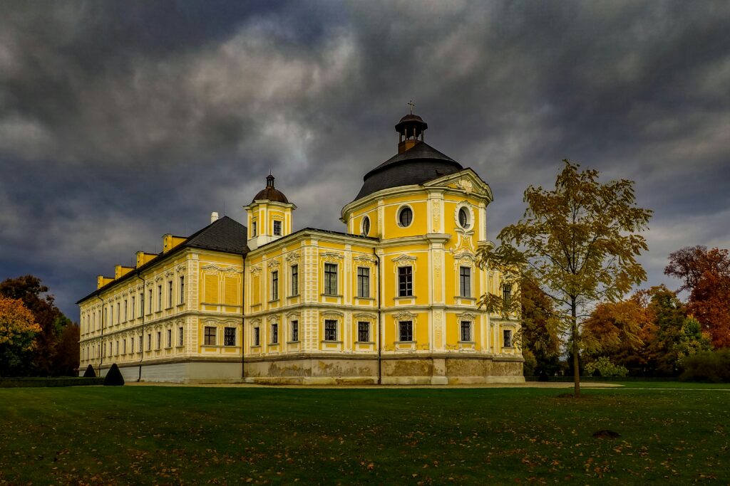 A Czech chateau that is painted pastel yellow and white under a stormy sky in Kravaře. Wheely Tyred Czech Silesia attractions