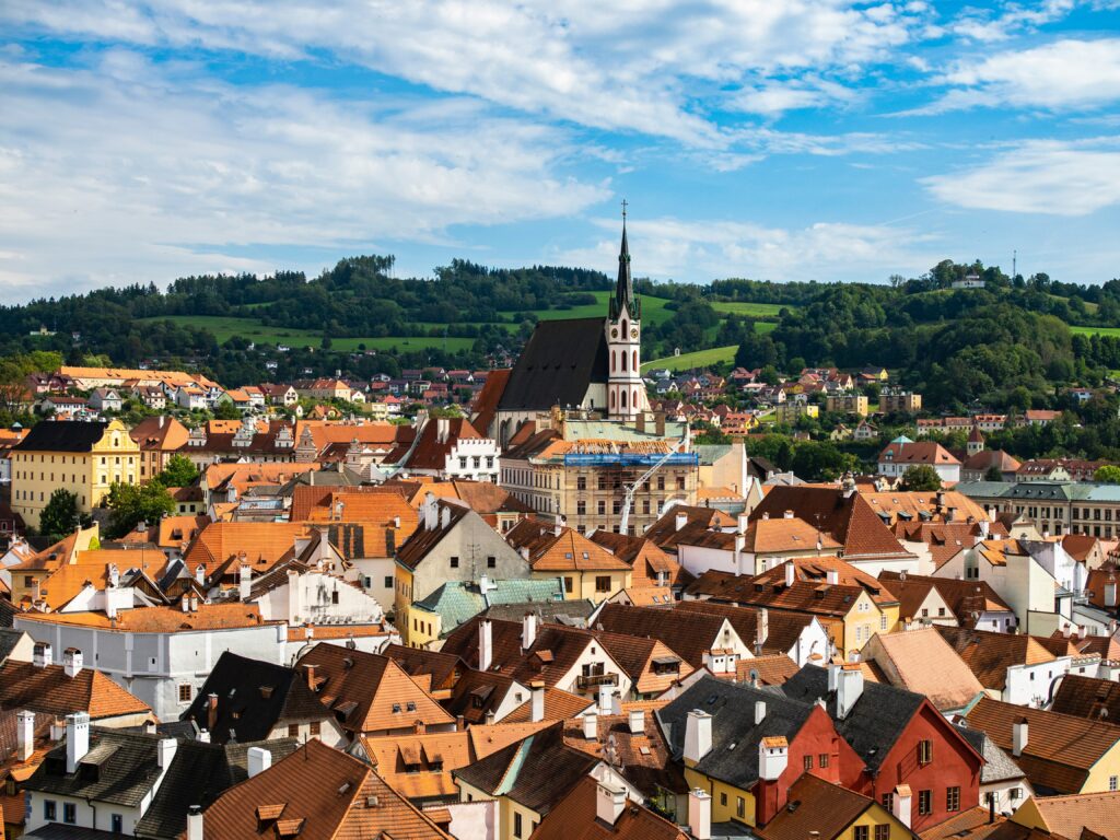 The old St. Vitus Church and tower rise above a city of red-roofed buildings 