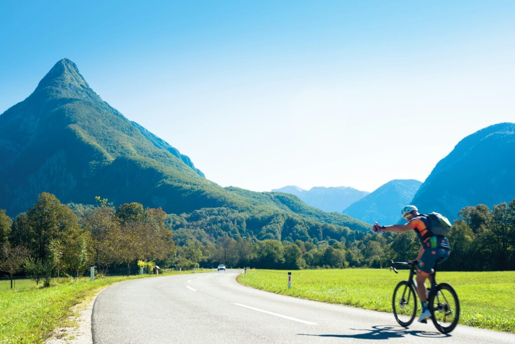 A person bikepacks along a flat road towards a large mountain on a bright day. Wheely Tyred cycling laws Czechia