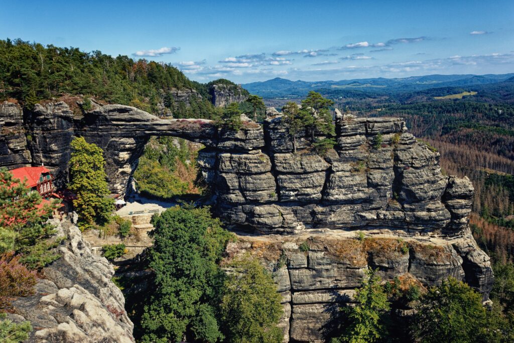 Rock formations and arches surround a chalet and are covered in fir trees at Prebischtor Gate, Hřensko. Wheely Tyred top attractions in Bohemia