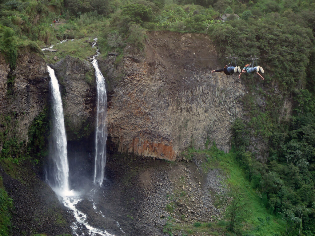 Two people slide along a zipline towards the Manto de la Novia waterfalls in Baños, Ecuador.