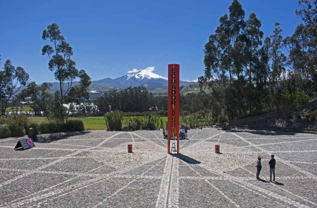 A large orange monument on the equator in Cayambe, Ecuador, with Cayambe Volcano behind