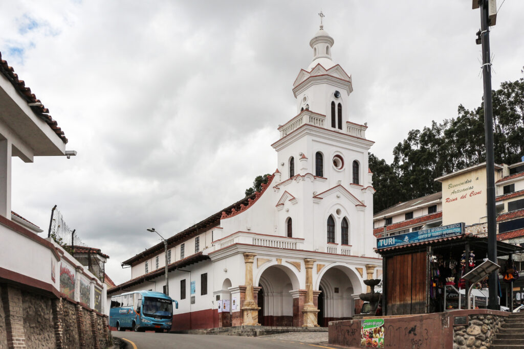 The white Turi Church stands on tops of a hill surrounded by forest.