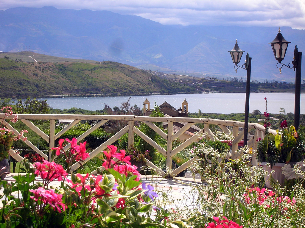 A panorama of the shores of Yahuarcocha during the summer season. Flowers and a church are in the foreground. Wheely Tyred Top sights in Ibarra