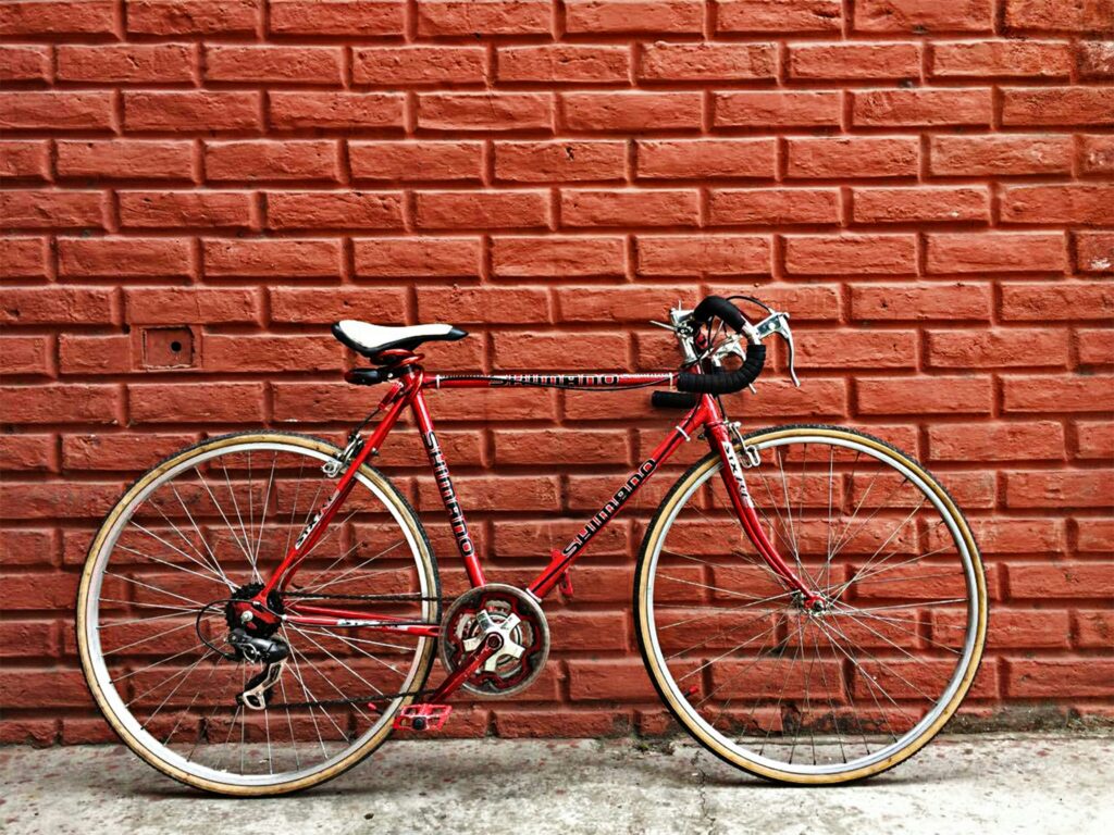 An old red road bike leans against a red brick wall in Guayaquil, Ecuador.