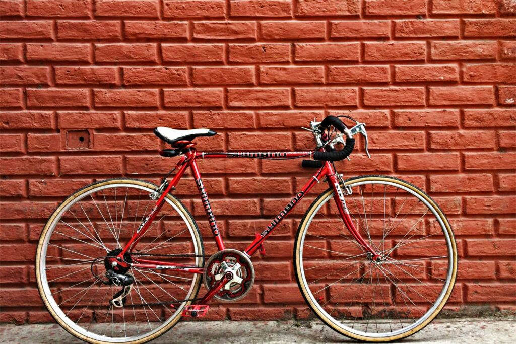 An old red road bike leans against a red brick wall in Guayaquil, Ecuador.