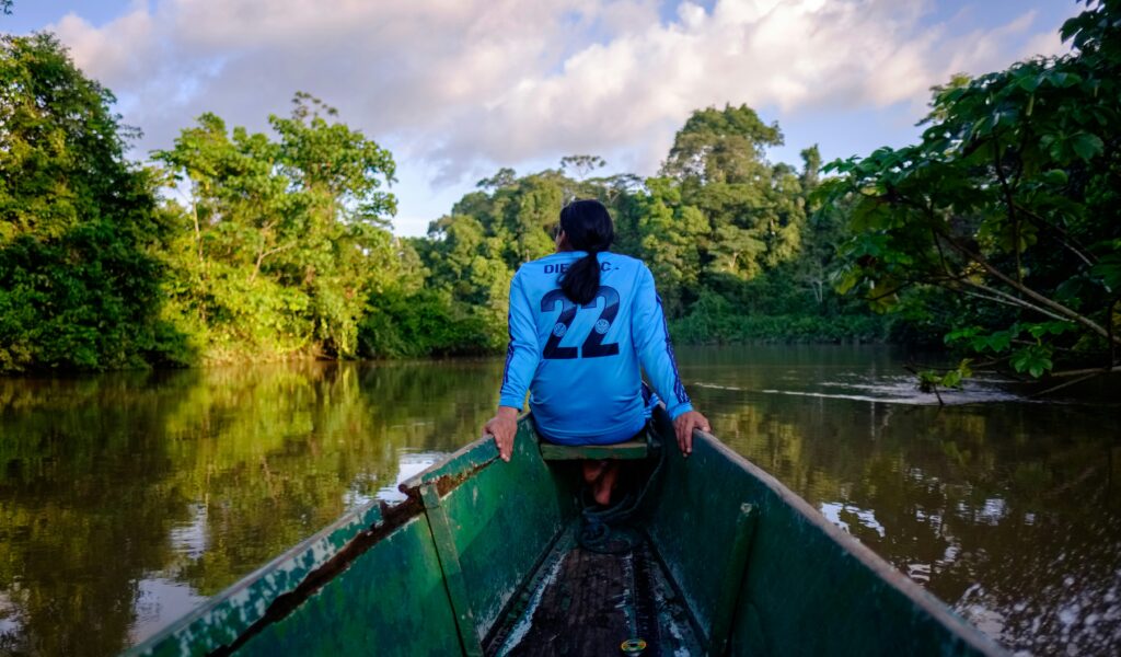 A man rides on the front of a canoe on a river in the Amazon of Ecuador