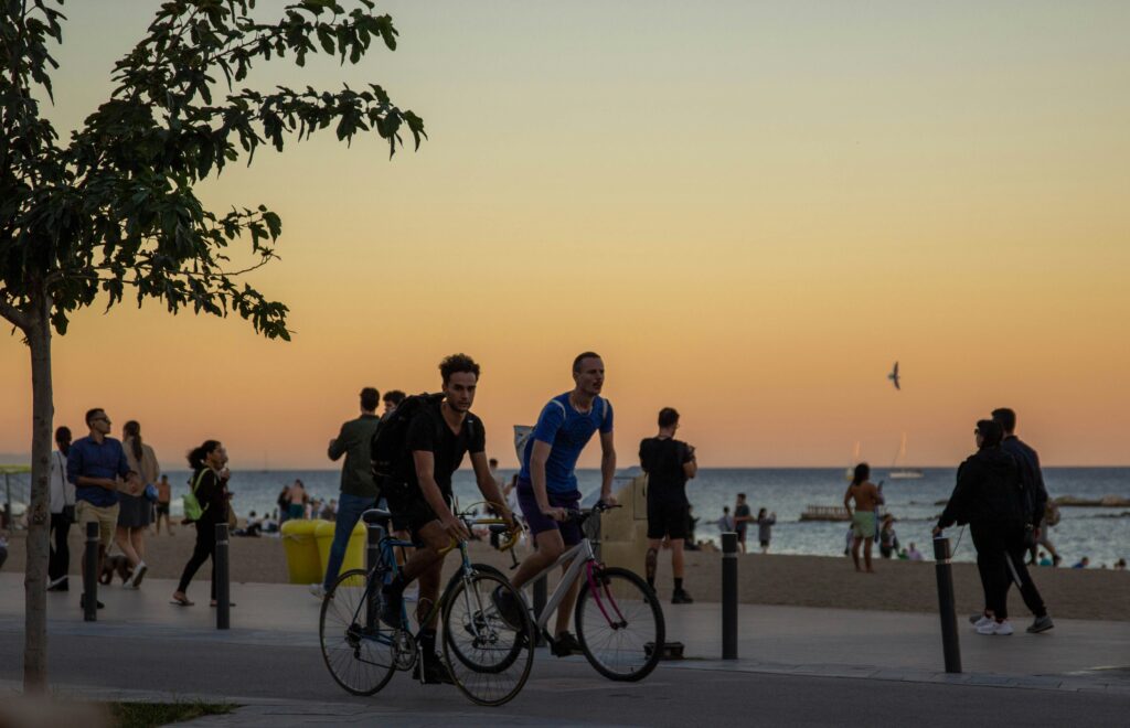 Two men ride bikes along La Barcelonetta in Barcelona, Spain, at sunset. Wheely Tyred barcelona beat traffic