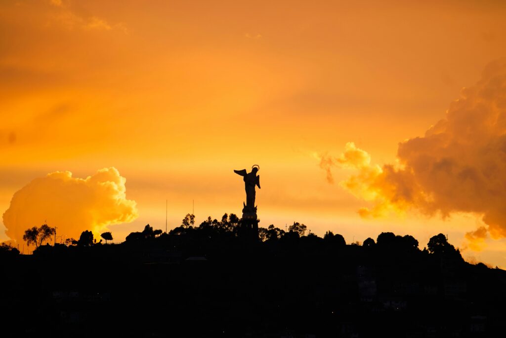 The Virgin of Quito on El Panecillo, wurrounded by an orange sky at sunset.