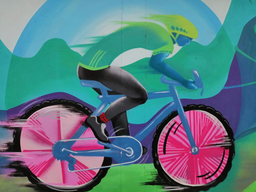 Street art of a road cyclist in Quito, Ecuador. The wheels are pink and the rider is in green.