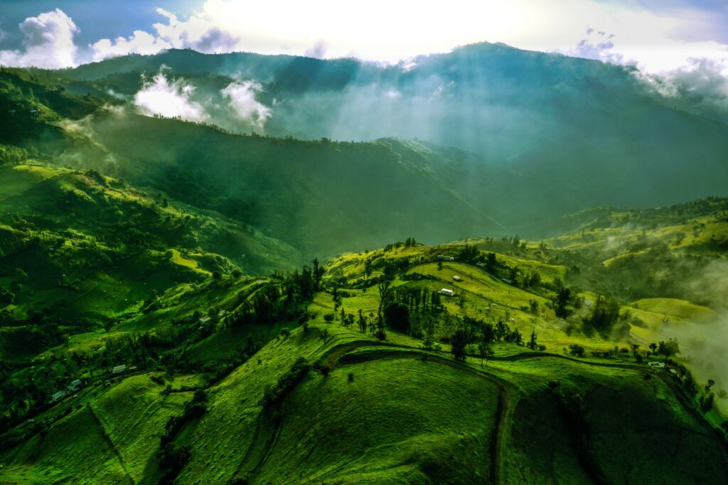 The sun breaks through clouds over the green fields of the Andes near Pinllopata, Ecuador.