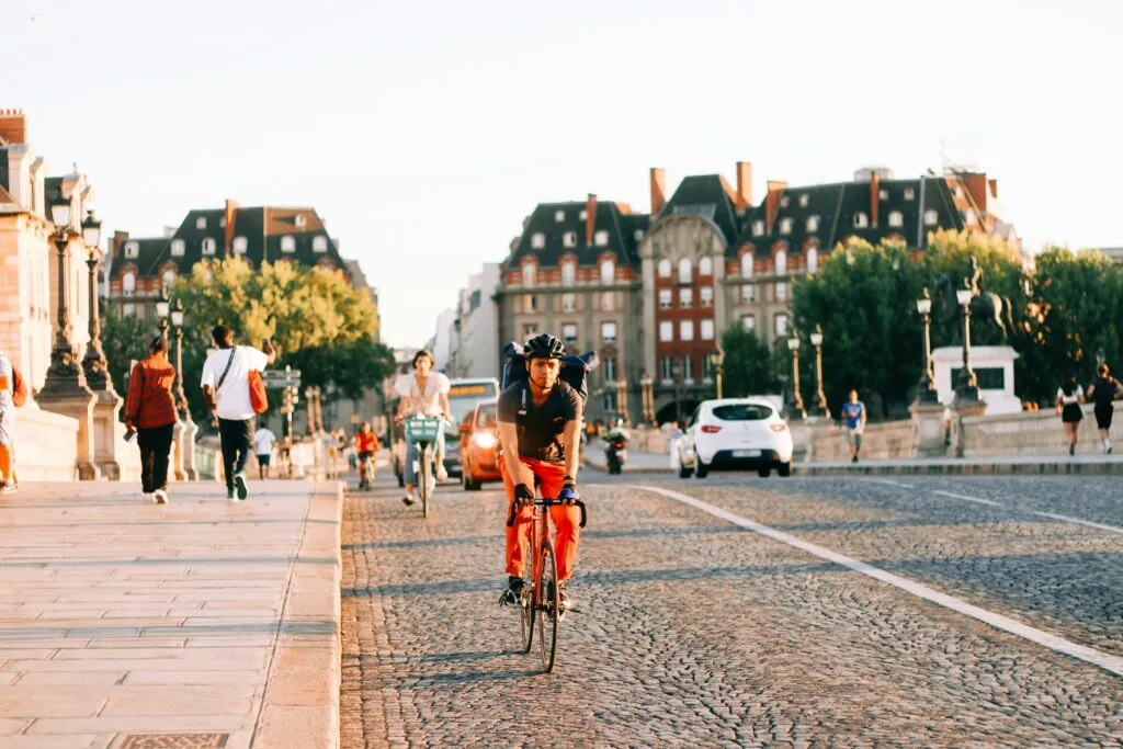 A cyclist rides a road bike along a cobbled street in Paris, France. There are many more cyclists following.