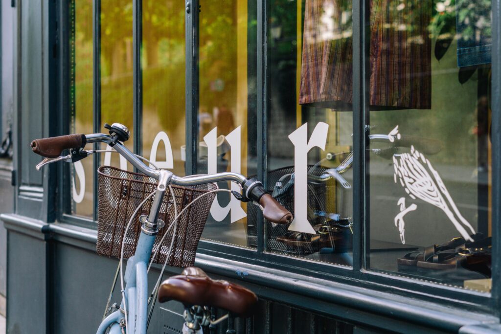 A vintage bicycle with a basket leans against the window of a bakery in Paris, France. Wheely Tyred Paris cycling transformation