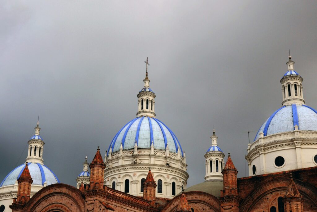 Dark clouds gather over the blue and white domes of the second cathedral in Cuenca, Ecuador.