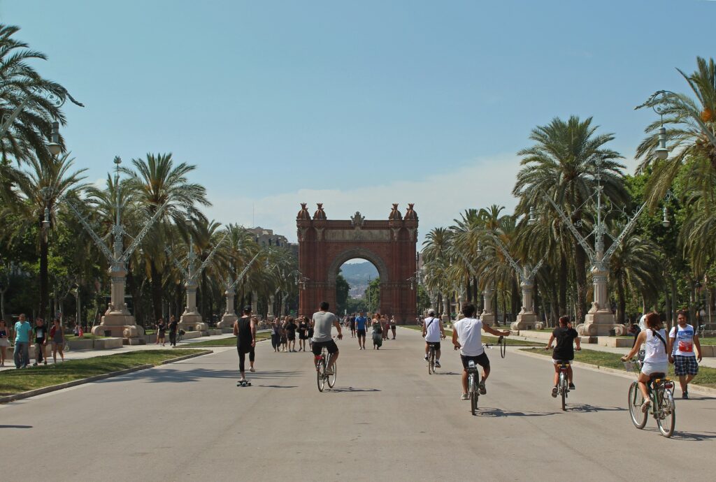 Cyclists ride towards the Arc de Triomf in Barcelona, Spain, on a sunny day.