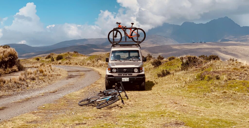 Mountain bikes lie in front of a Toyota pickup. There's on on e the roof too. The foothills of Cotopaxi surround the truck
