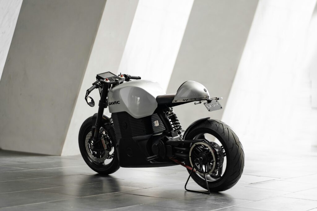 A sleek white e-moto against a grey background in a press shot. Wheely tyred E-motos and e-bikes