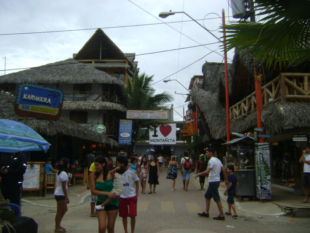 People walk along a busy street under a sign that reads "I love Montañita" in Ecuador.
