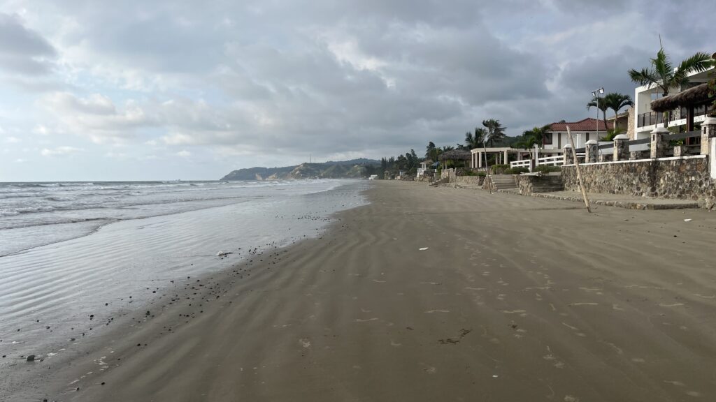 Playa Olón on a pretty dull day. The ocean is calm, and beach houses are built along the side.