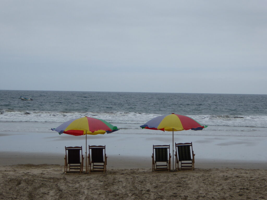 Two sets of beach chairs sit on the beach under umbrellas facing the sea.