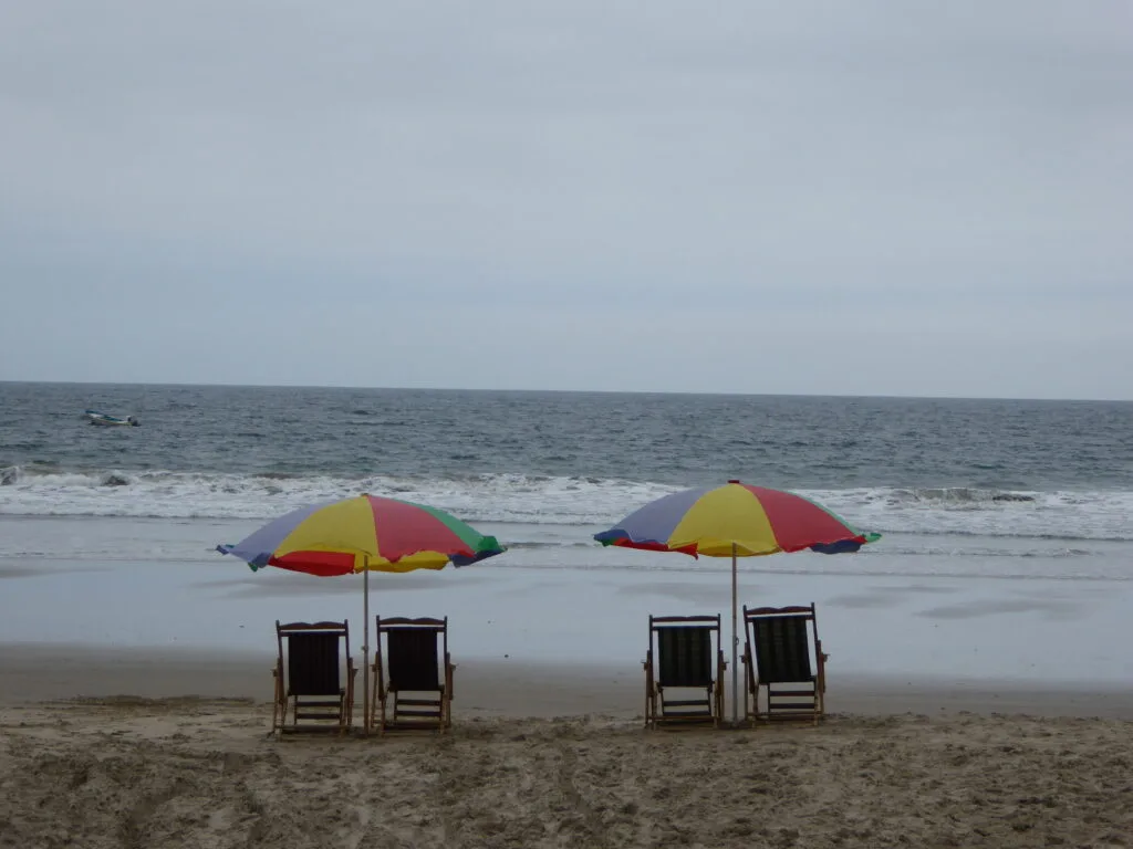 Two serts of deckchairs sit under parasols on the beach in Montanita, Ecuador. Wheely Tyred Ecuadorian Coast