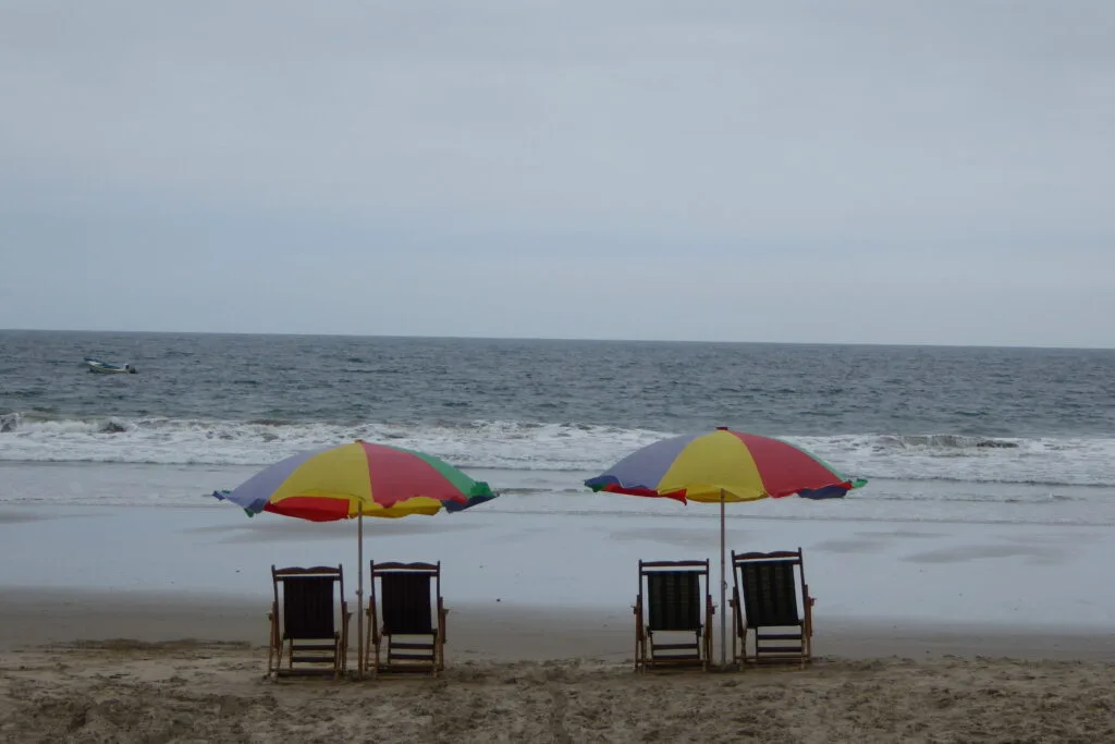 Two serts of deckchairs sit under parasols on the beach in Montanita, Ecuador/