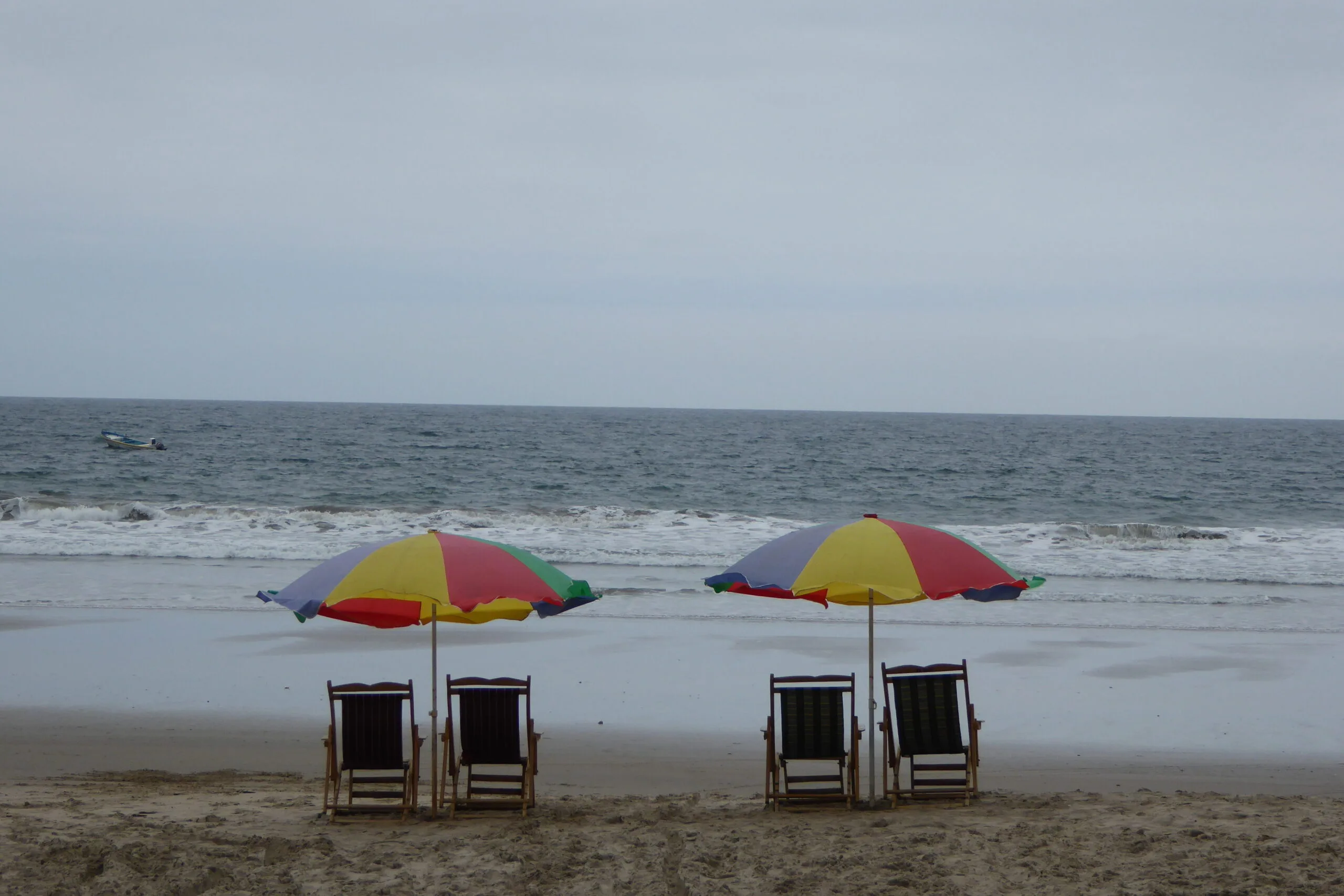 Two serts of deckchairs sit under parasols on the beach in Montanita, Ecuador/