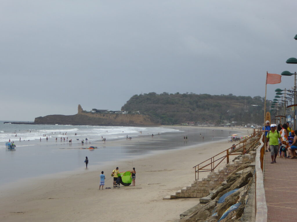 People play and walk along the beach in Ecuador. There's a paved promenade above it. Wheely Tyred Montañita safety