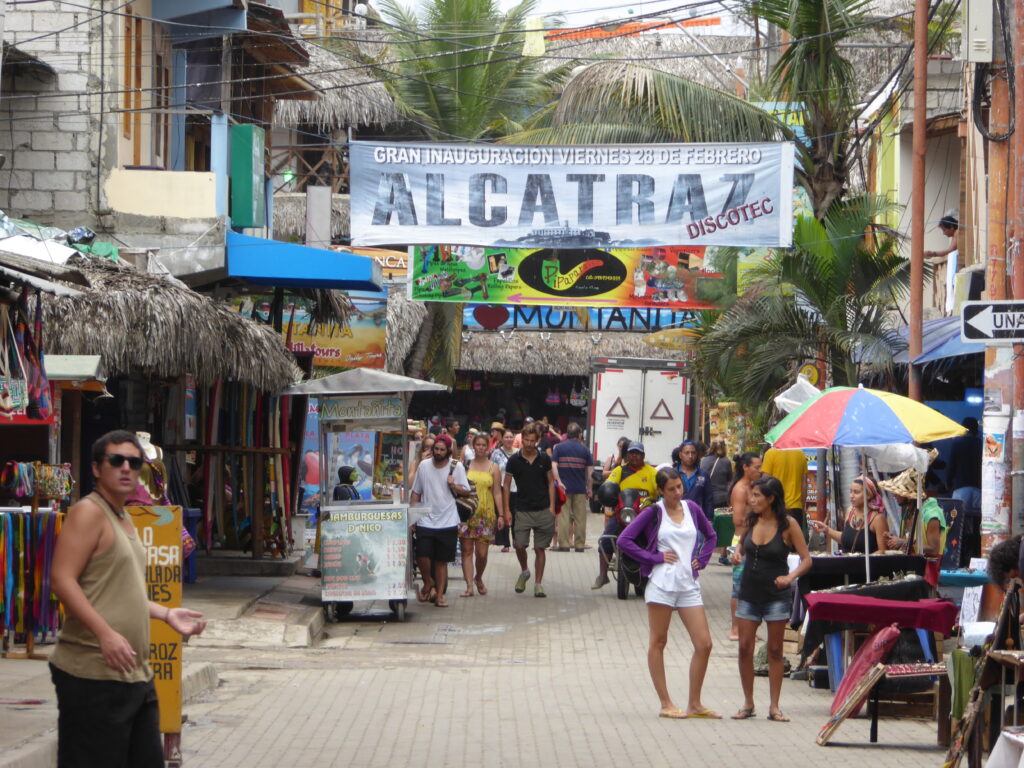 Tourists walk along a street in Montañita, Ecuador, under a sign advertising a new nightclub.