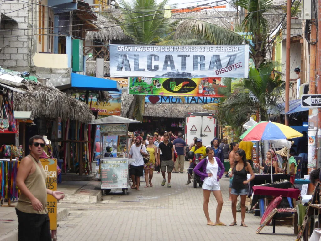 Tourists walk along a street in Montañita, Ecuador, under a sign advertising a new nightclub.
