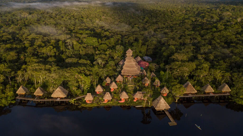 An aerial shot of the Napo Wildlife Center Ecolodge showing the complex of thatched roofs between a lake and the jungle in Yasuní, Ecuador.