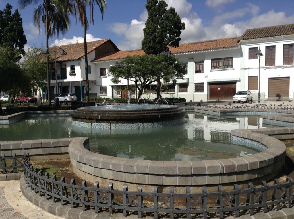 A fountain sits in front of a large white church in Plaza de San Sebastian in Cuenca, Ecuador