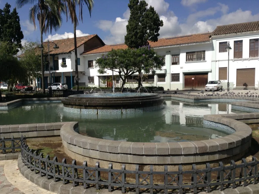 A fountain sits in front of a large white church in Plaza de San Sebastian in Cuenca, Ecuador