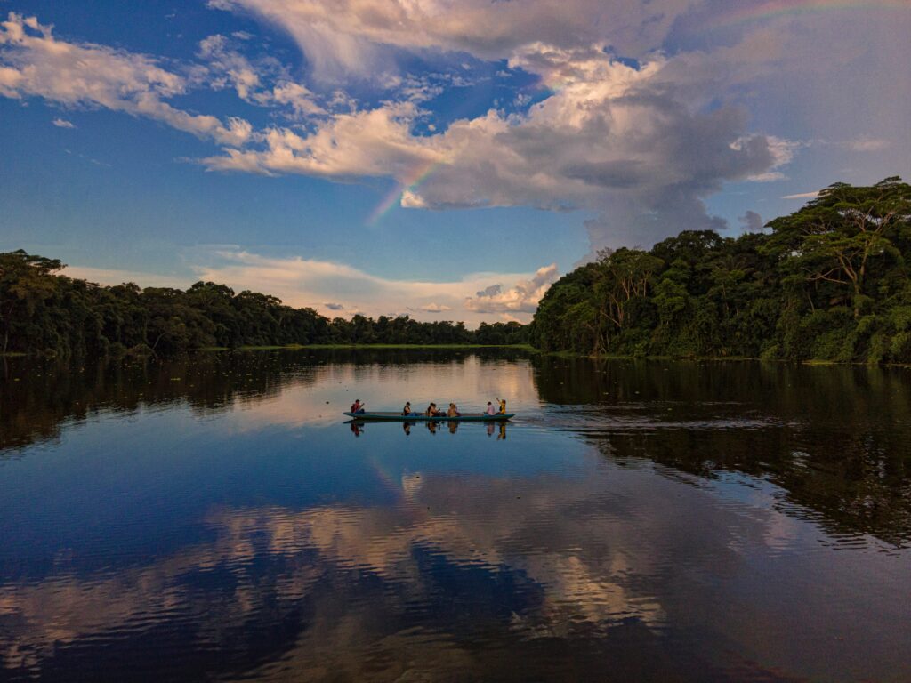 A kayak floats in a river. The jungle and sky are reflected in the still water. Wheely Tyred Ecuadorian Amazon safety