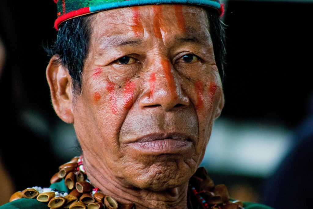 An indigenous man looks directly at the camera in traditional dress and paint in the Amazon, Ecuador.