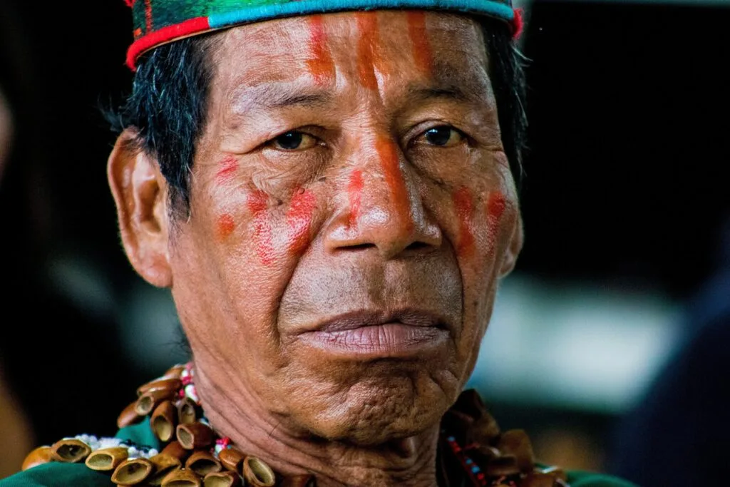 An indigenous man looks directly at the camera in traditional dress and paint in the Amazon, Ecuador.