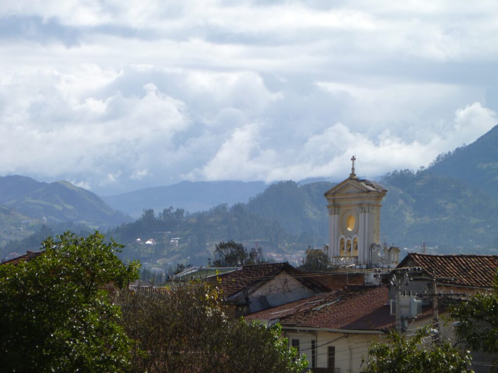 A small church tower rises in the foreground. In the distance behind it, there’s huge green valleys near Ecuador. Wheely Tyred history of Cuenca